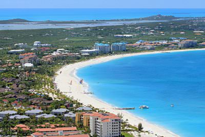 Aerial view of Grace Bay Beach in Providenciales with turquoise water, white sand, resorts, and boats along the Turks and Caicos coastline.