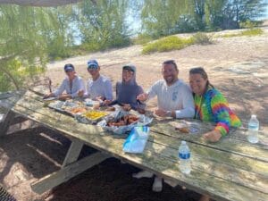 Beach BBQ on a Private Snorkeling Charter in Turks and Caicos Guests enjoying an optional beach BBQ lunch at a sandy picnic table during a private snorkeling charter day in Turks and Caicos